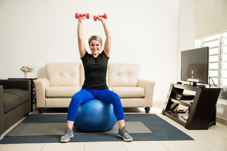 Woman sitting on stability ball with dumbbells in hands