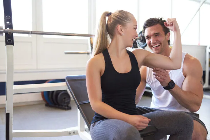 Woman flexing biceps with personal trainer